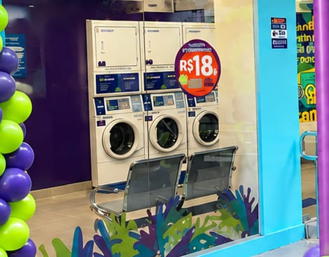 Vitrine da Lavô Pina vista da calçada, com as máquinas ao fundo e o adesivo de R$ 18